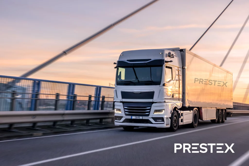 um caminhão branco com o semirreboque logotipado 'Prestex' trafega sobre uma ponte
